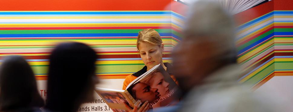 Verschwommen sichtbare Menschen gehen an einer lesenden Frau vorbei