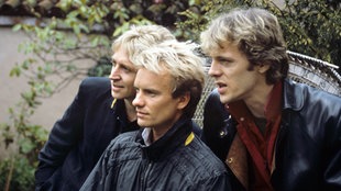 Die Band The Police sitzen auf einer Bank in einem Garten