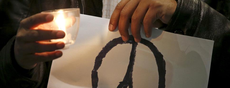 Ein Mann hält ein Blatt Papier in der Hand, darauf ist ein "Peace"-Zeichen mit einem Eiffelturm zu sehen