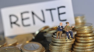 ILLUSTRATION - Miniatur-Figuren zweier Rentner sitzen auf Münzen vor einem Schild mit der Aufschrift "Rente".