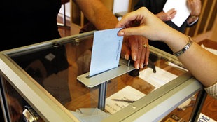 Eine Frau wirft einen Stimzettel in eine Wahlurne aus Glas