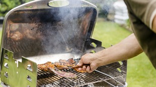Ein Mann steht an einem Grill und wendet das Fleisch