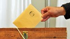 Ein Mann wirft einen Stimmzettel im Umschlag in die Wahlurne
