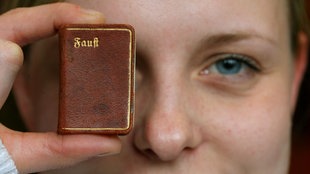 Frau hält klein Buch, Augen im Hintergrund