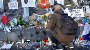 Ein junger Mann mit Kopfhörern hockt vor einem Meer von Kerzen, Blumen und Schildern