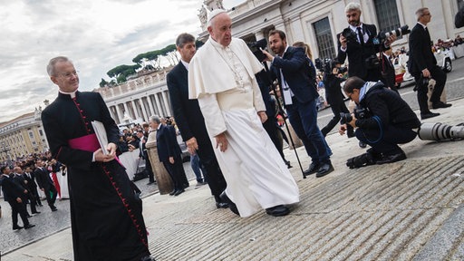 Papst Franziskus ist auf dem Weg zur wöchentlichen Audienz auf dem Petersplatz umringt von Kardinälen, Bediensteten und Fotografen.