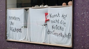 Plakat im Fenster mit der Aufschrift: Kunst ist nicht die Krücke der Gesellschaft sondern ihr Rückgrat